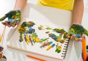 criança pintando as mãos e o papel com tintas coloridas