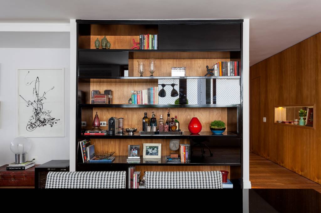 estante de madeira Na foto, aparece estante de madeira com portas pretas. Há vários objetos na estante, como livros, vasos e enfeites
