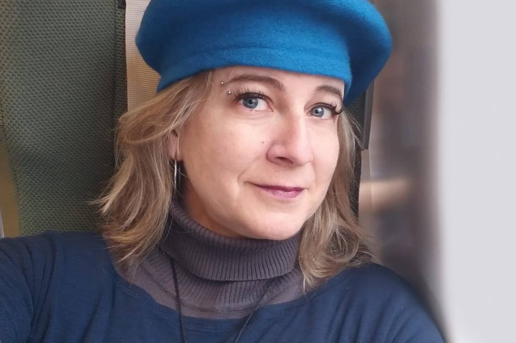Voluntária Tatiana Ferraz Vacina Covid Selfie de mulher branca, com cabelos loiros curtos. Ela usa uma boina azul e uma blusa da mesma cor