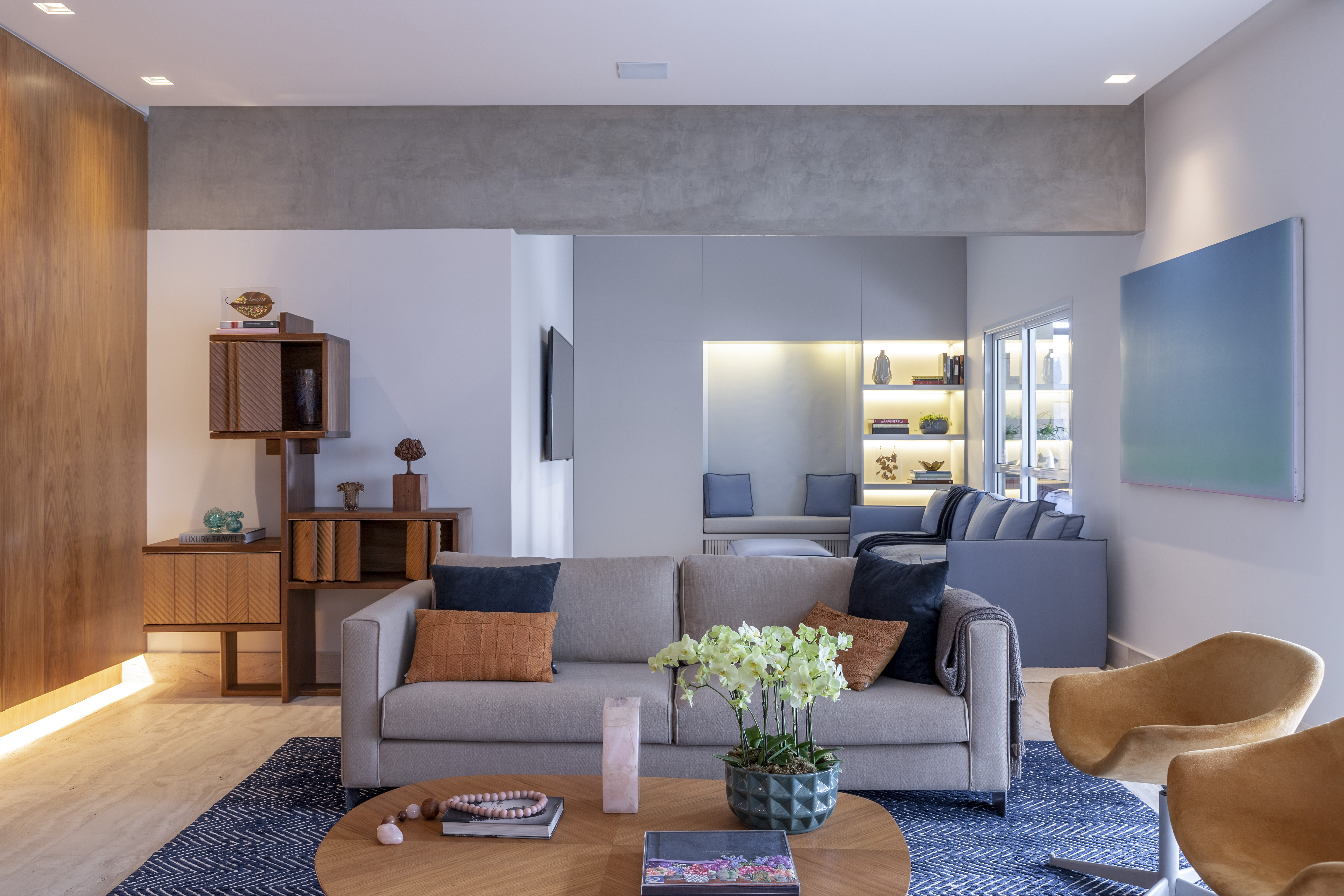 Sala de estar integrada com sof&aacute; cinza, tapete azul e mesa de madeira