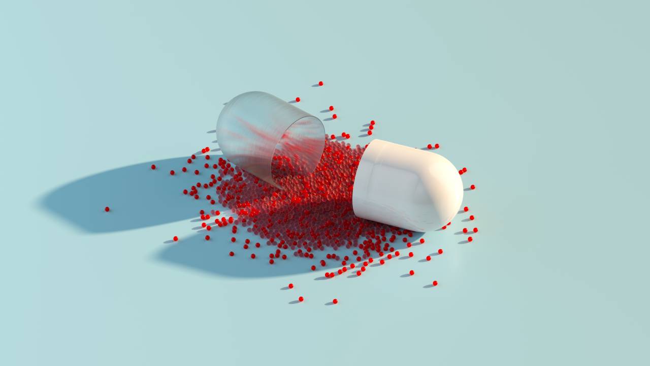 Digital generated image of abstract opened plastic capsule pill with small red spheres inside on pastel blue background.