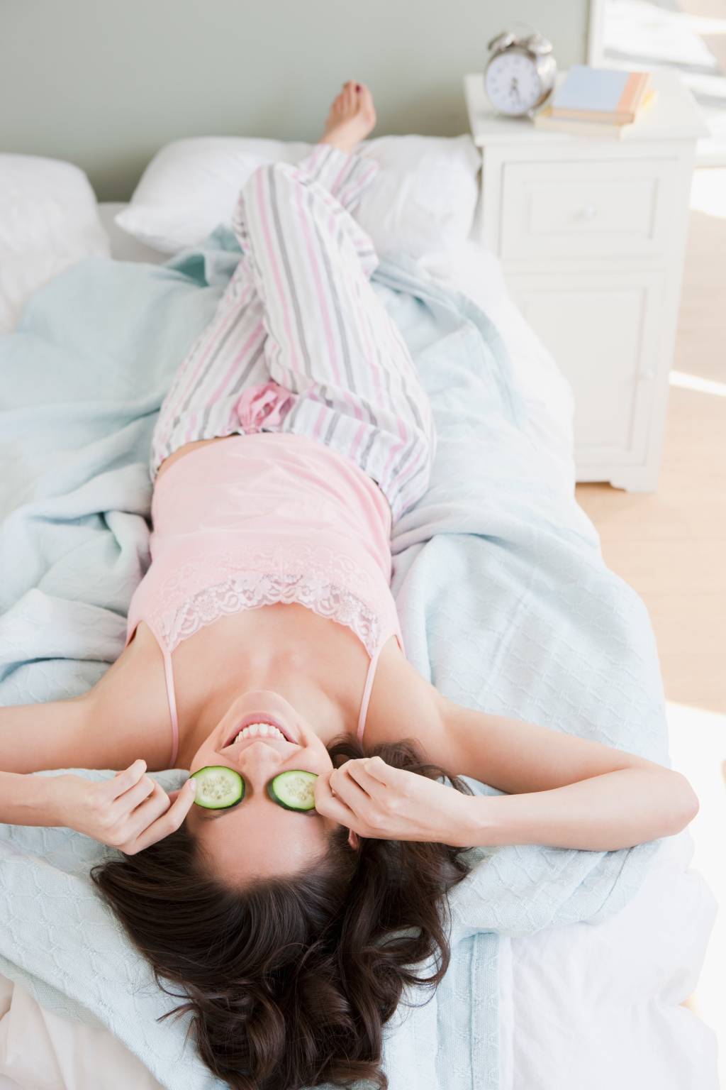 Mixed race woman placing cucumbers over eyes in bed Mixed race woman placing cucumbers over eyes in bed