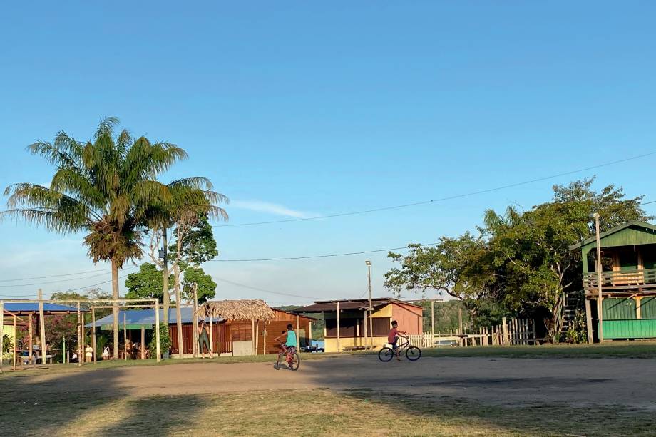 Duas crianças pedalam numa clareira da comunidade de Tumbira, formada por casas de madeira multicoloridas.