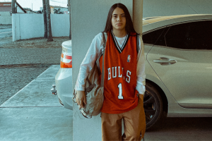 Mulher vestindo camisa de time de basquete com calça de alfaiataria bege, dentro da tendência blokecore