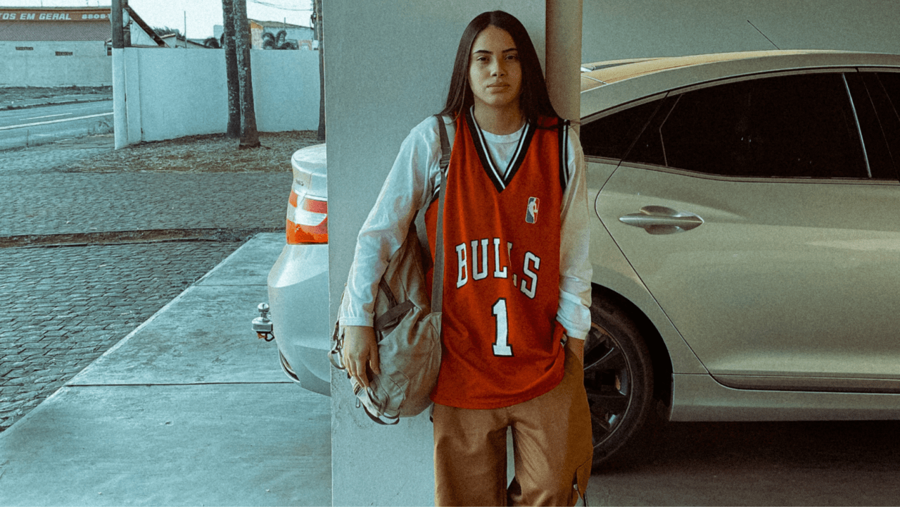 Mulher vestindo camisa de time de basquete com calça de alfaiataria bege, dentro da tendência blokecore