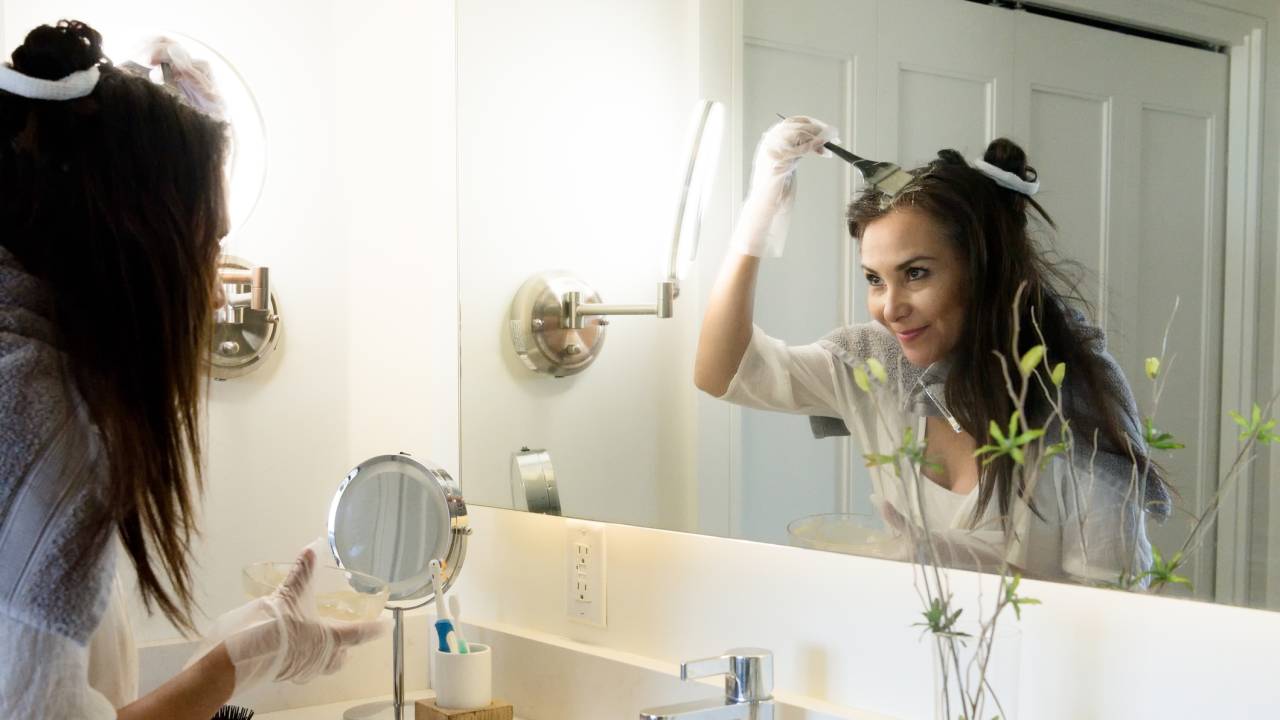 Mulher madura tingindo o cabelo no banheiro de casa.