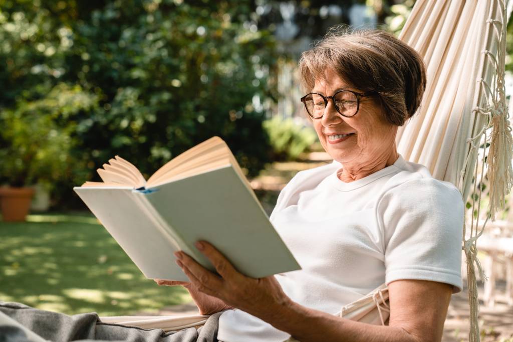 livros-dia-das-maes-ideias-para-presentear Mulher madura lendo um livro no jardim de sua casa.