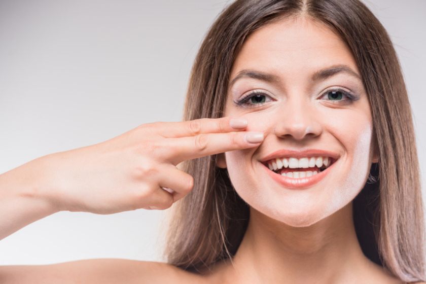 Imagem de mulher sorrindo com dois dedos apontado para o rosto