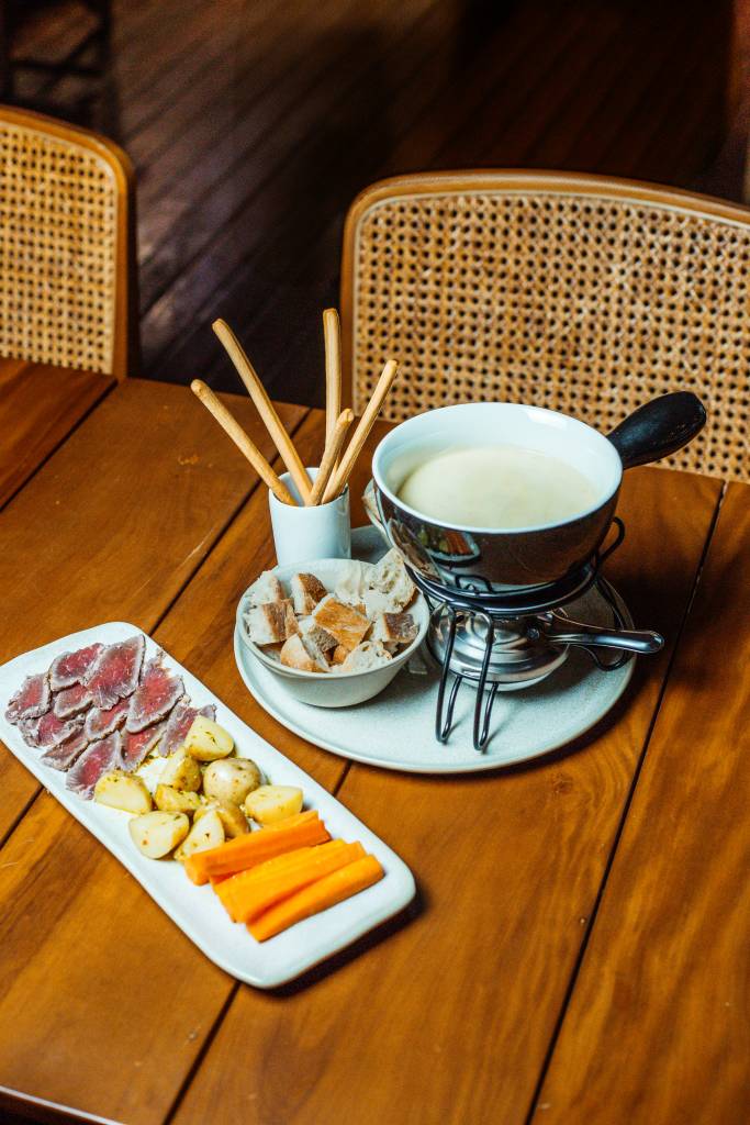 Fondue Cabruca O restaurante, que fica dentro da fábrica da Dengo, é uma ótima opção para o fim de semana – já que, além da refeição, também é possível conhecer o processo de produção das barras bean-to-bar. Para começar, o local traz duas opções principais: o Fondue de Queijo Tradicional (R$ 129,90) e o Fondue de Queijo Vegano (R$ 129,90), ambos acompanhados de pães de fermentação natural, batata bolinha, grissini, cenoura e cogumelos portobello. Para uma experiência ainda mais especial, é possível adicionar acompanhamentos como carne de sol (R$ 149,90) ou frutos do mar (R$ 159,90).