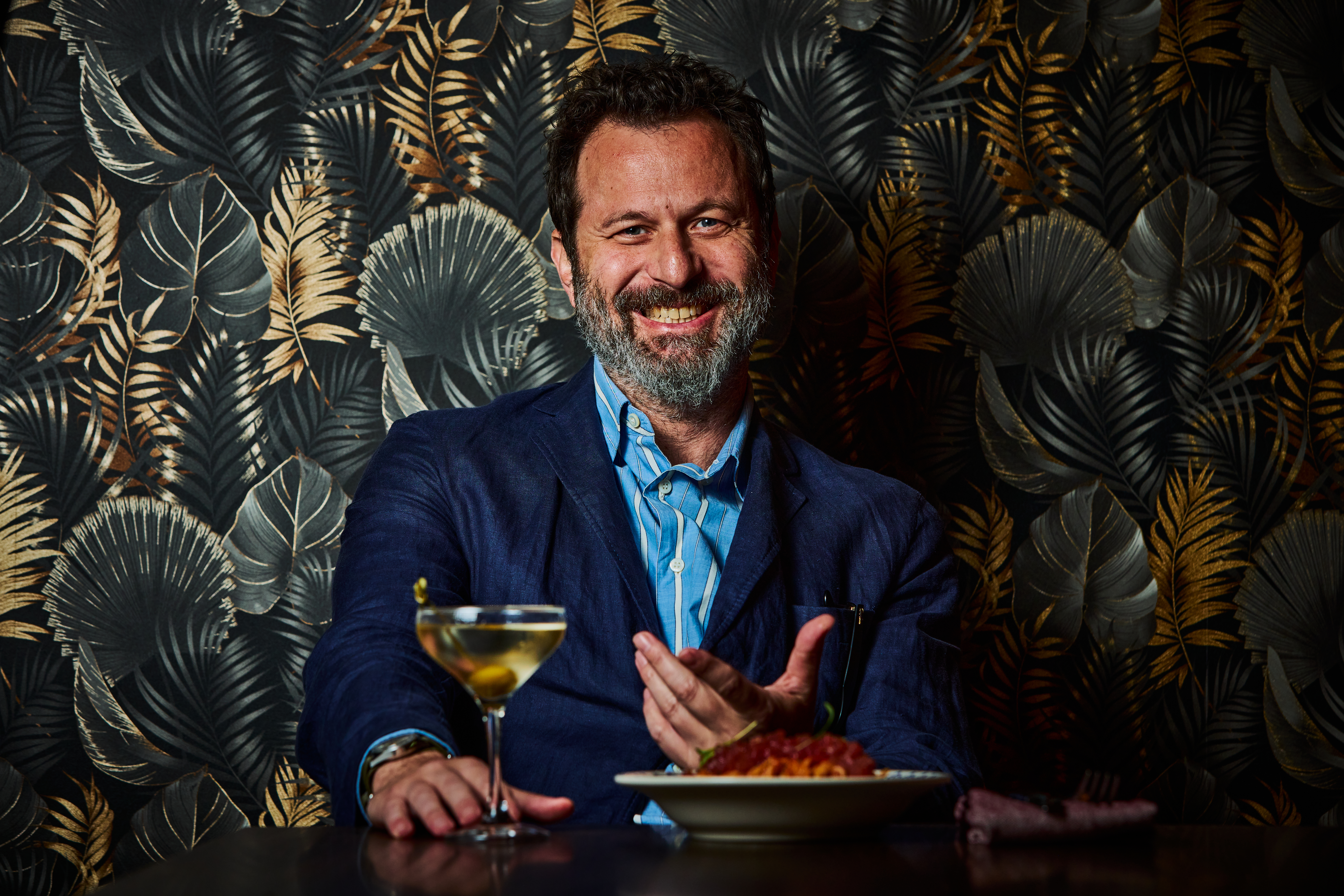 Imagem do mixologista Al&ecirc; D'Agostino visto de frente sentado, junto a um drink