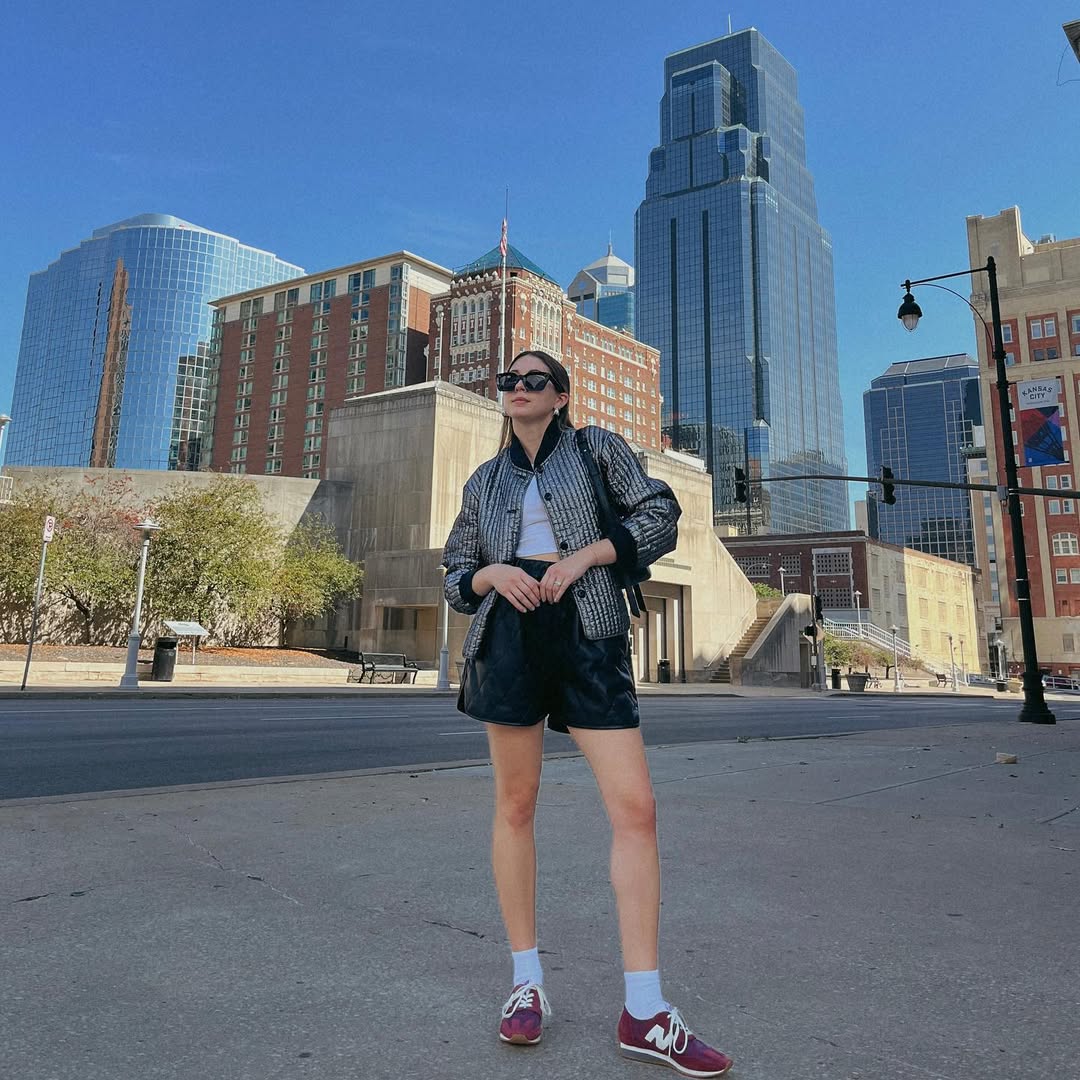 Foto de uma mulher usando um look composto por jaqueta preta, short de couro preto, t&ecirc;nis vinho e meia