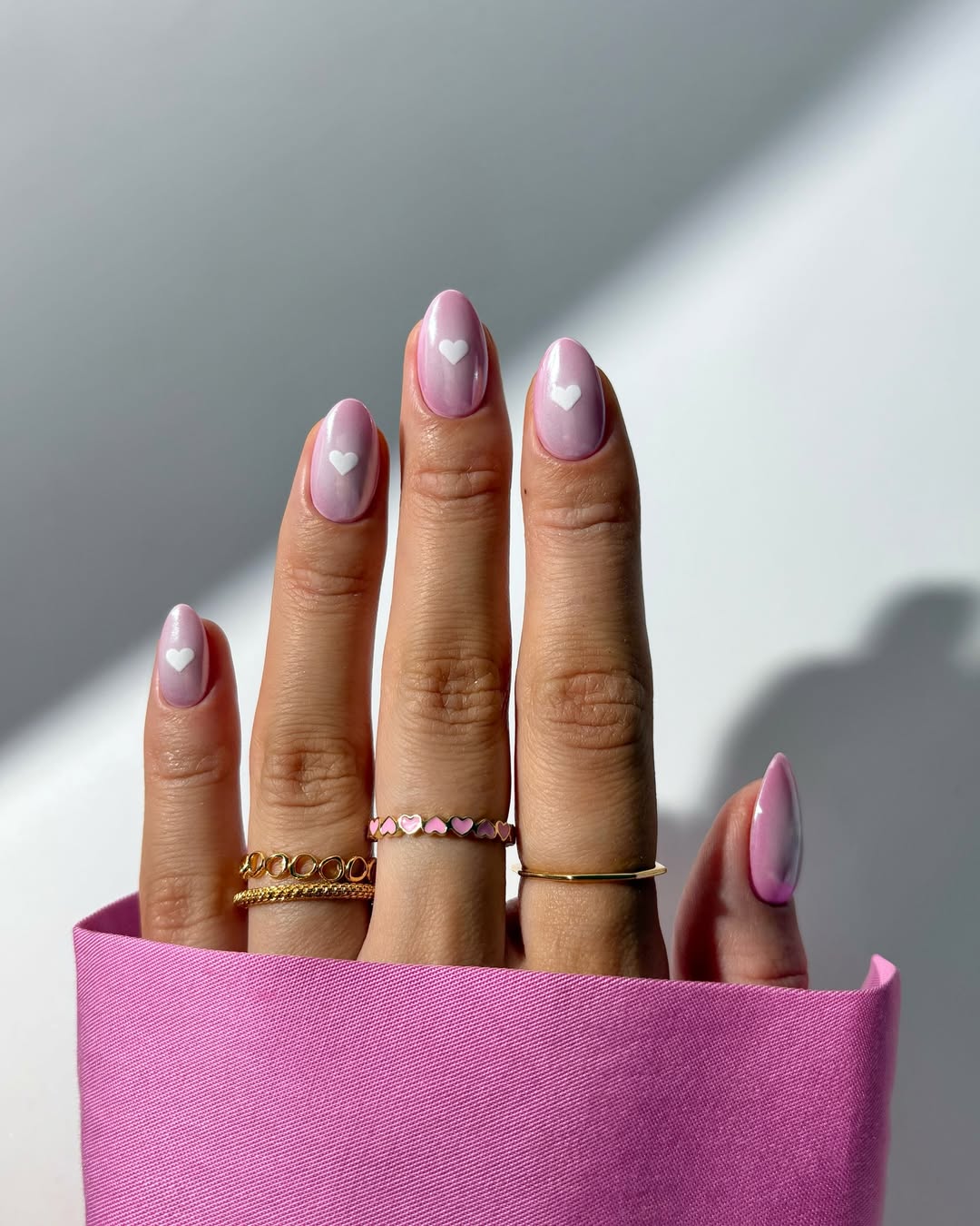 Imagem mostra unhas decoradas delicadas com esmalta&ccedil;&atilde;o rosa e branco, e cora&ccedil;&otilde;es.