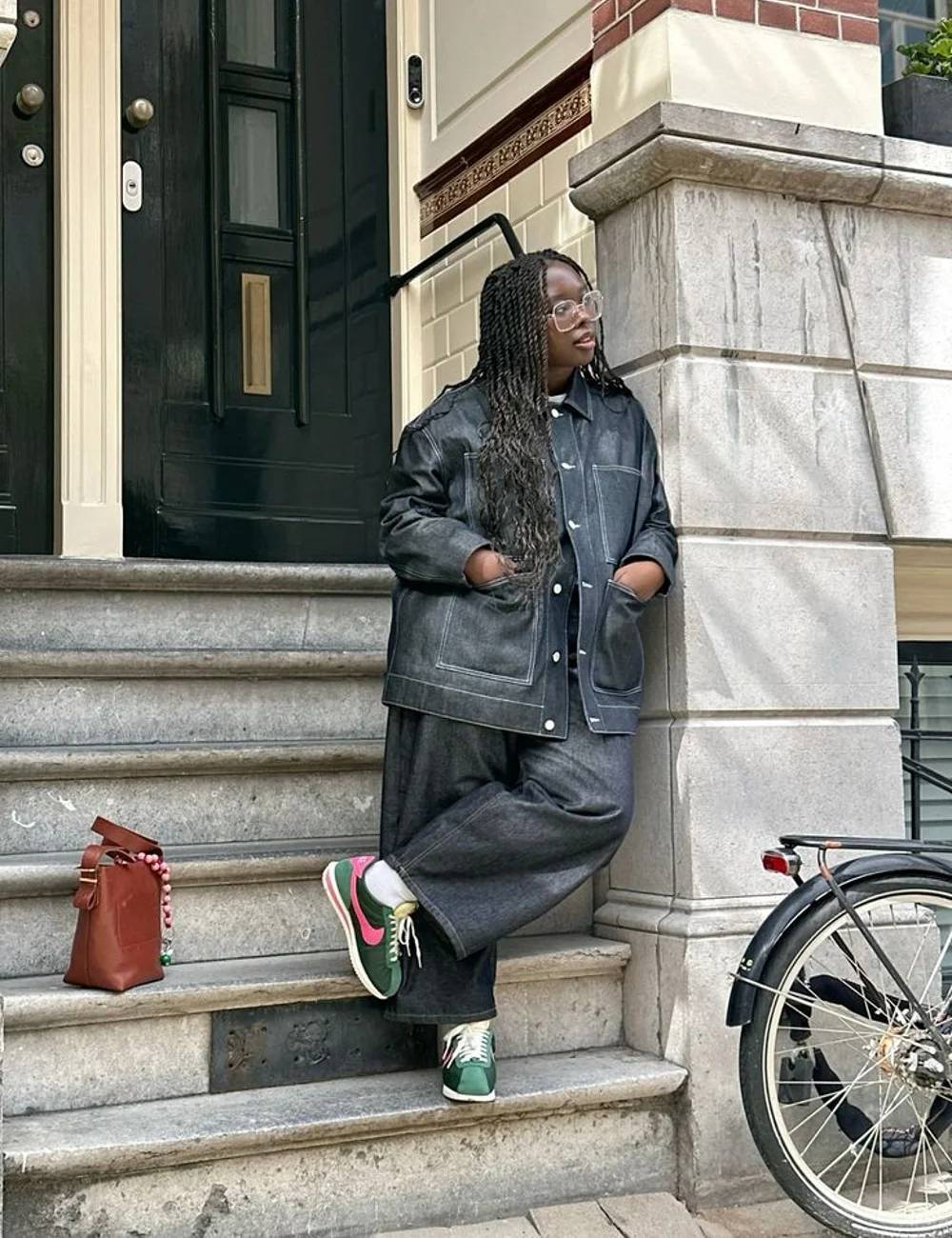 Foto de uma mulher negra usando um look composto por jaqueta jeans, calça jeans e calça verde pistache