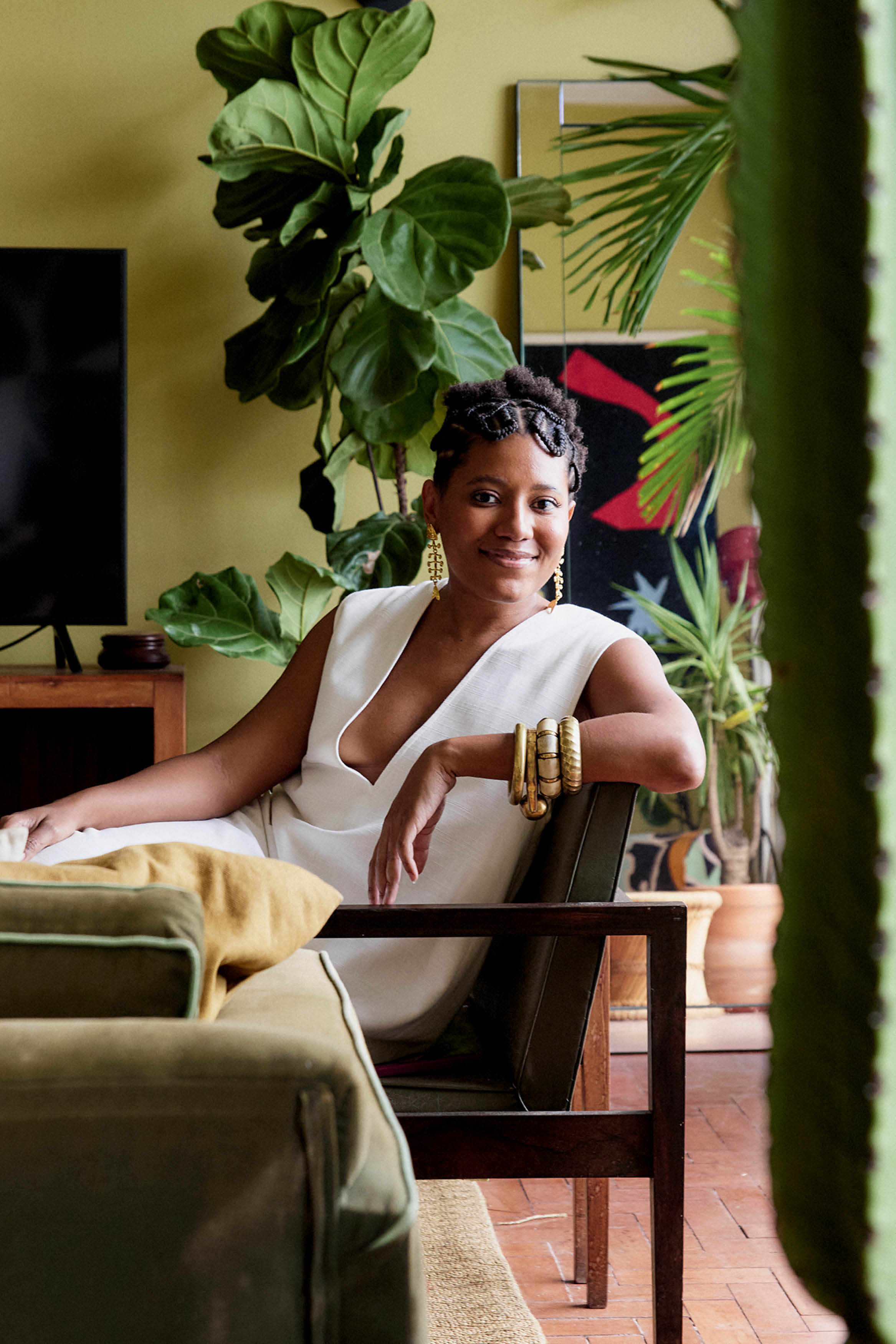 Mulher de vestido branco sentada em cadeira em casa com plantas.
