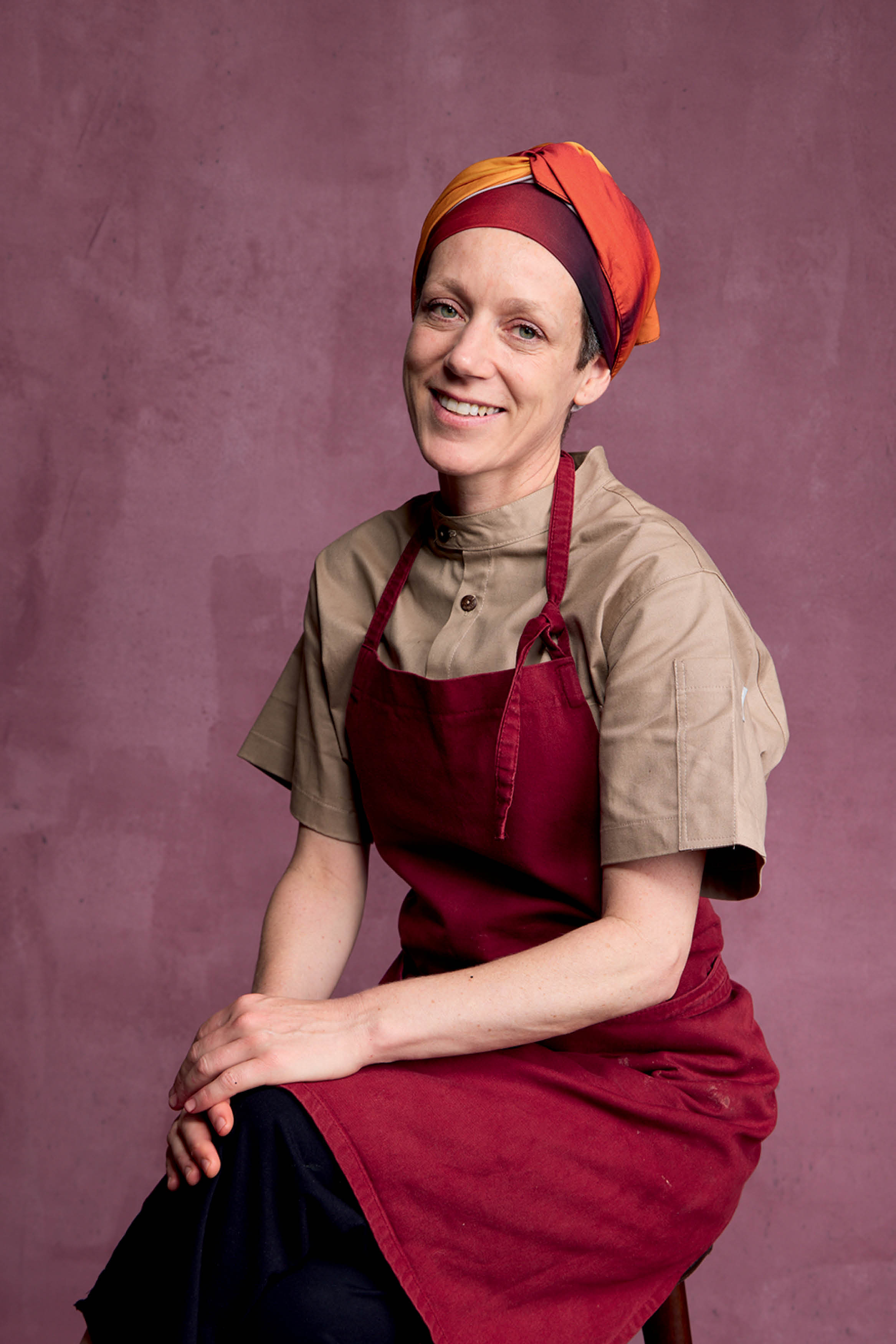 Chef de cozinha sentada em banco de est&uacute;dio sorrindo para foto.
