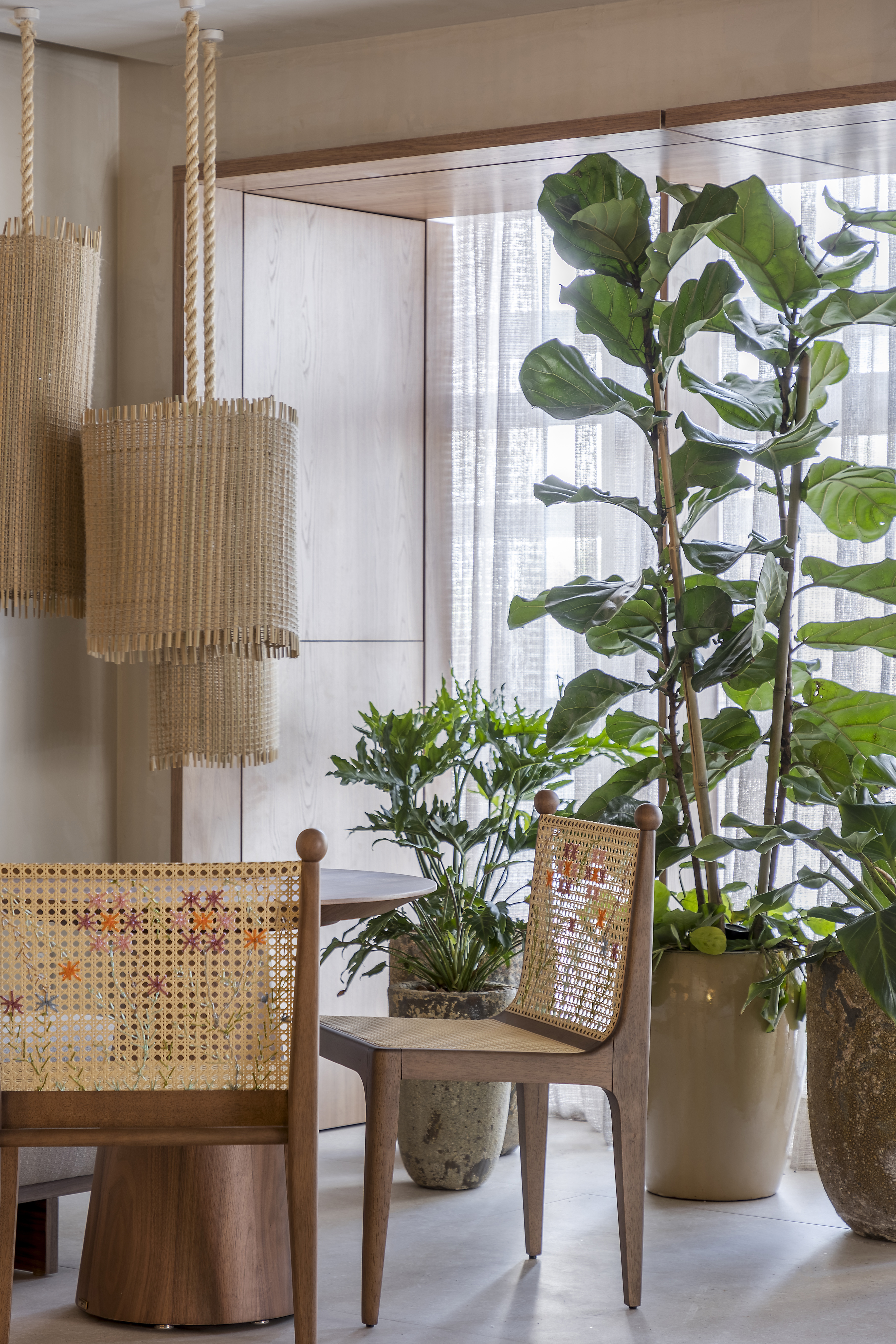 Canto de sala de estar com cadeiras de tela, abajur de palha e vasos de plantas