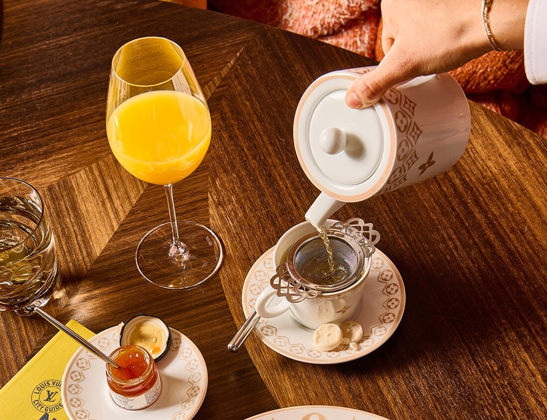 Pessoa servindo ch&aacute; em mesa com doce e suco de laranja