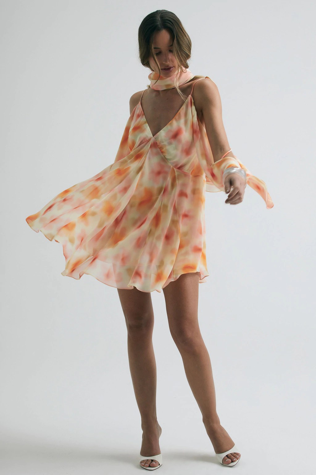 Foto de uma mulher branca usando um vestido fluido e estampado, al&eacute;m de um len&ccedil;o no pesco&ccedil;o