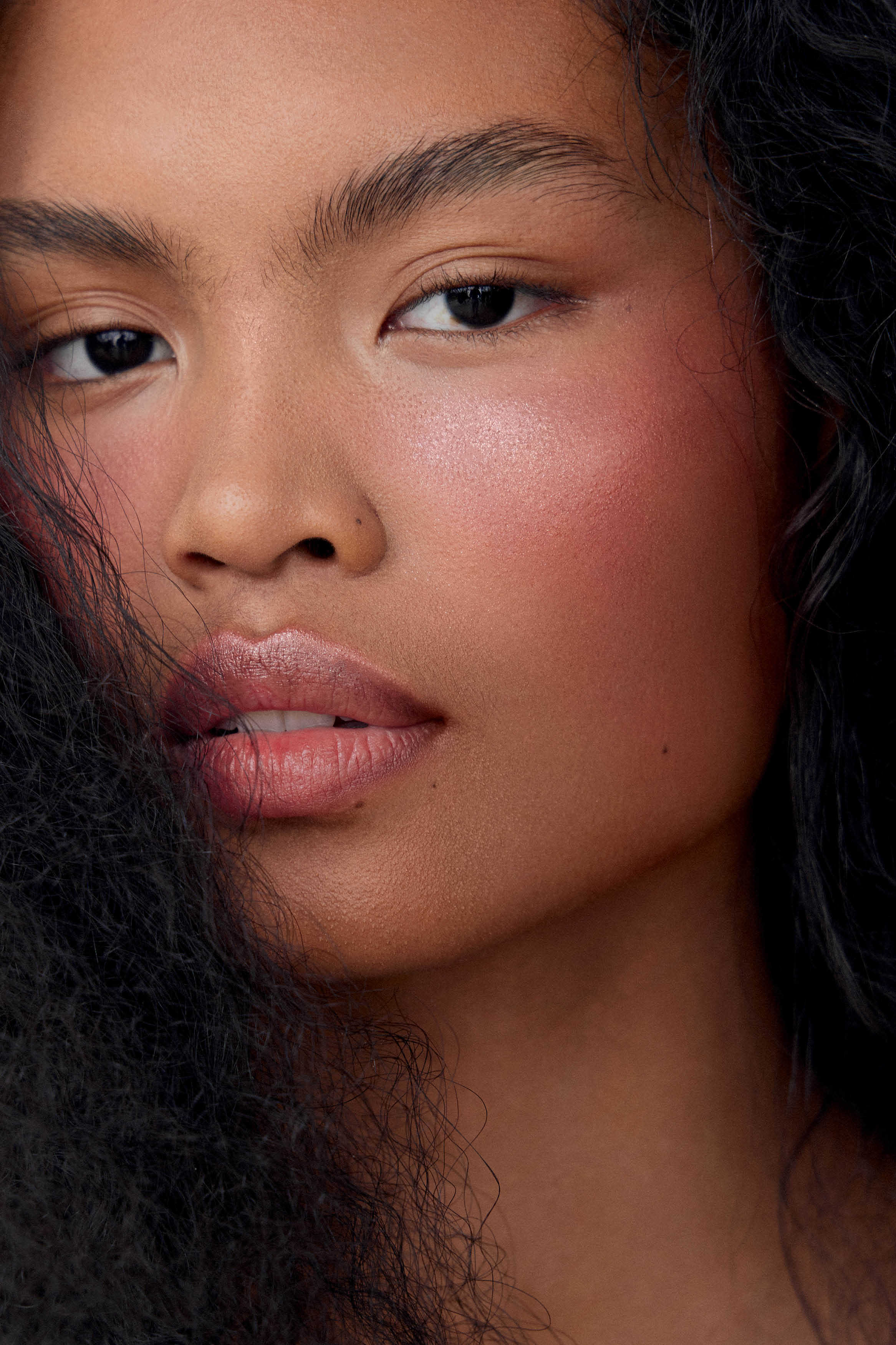 Close no rosto de modelo de pele negra com cabelos pretos soltos e maquiagem em tons rosados