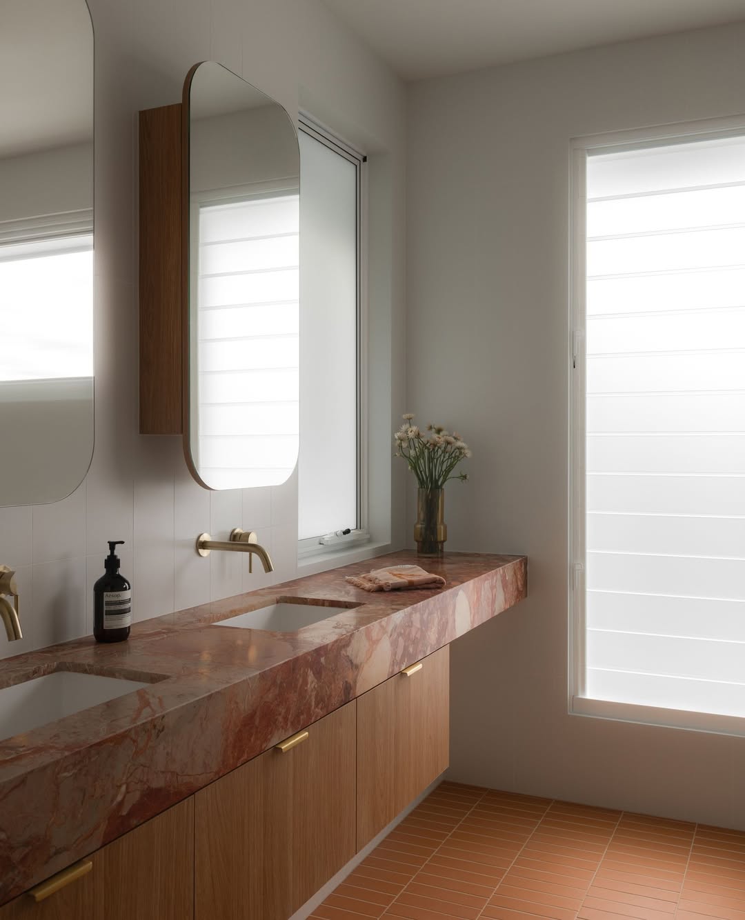 Banheiro com bancada de m&aacute;rmore vermelho, piso de cer&acirc;mica e cantos arredondados