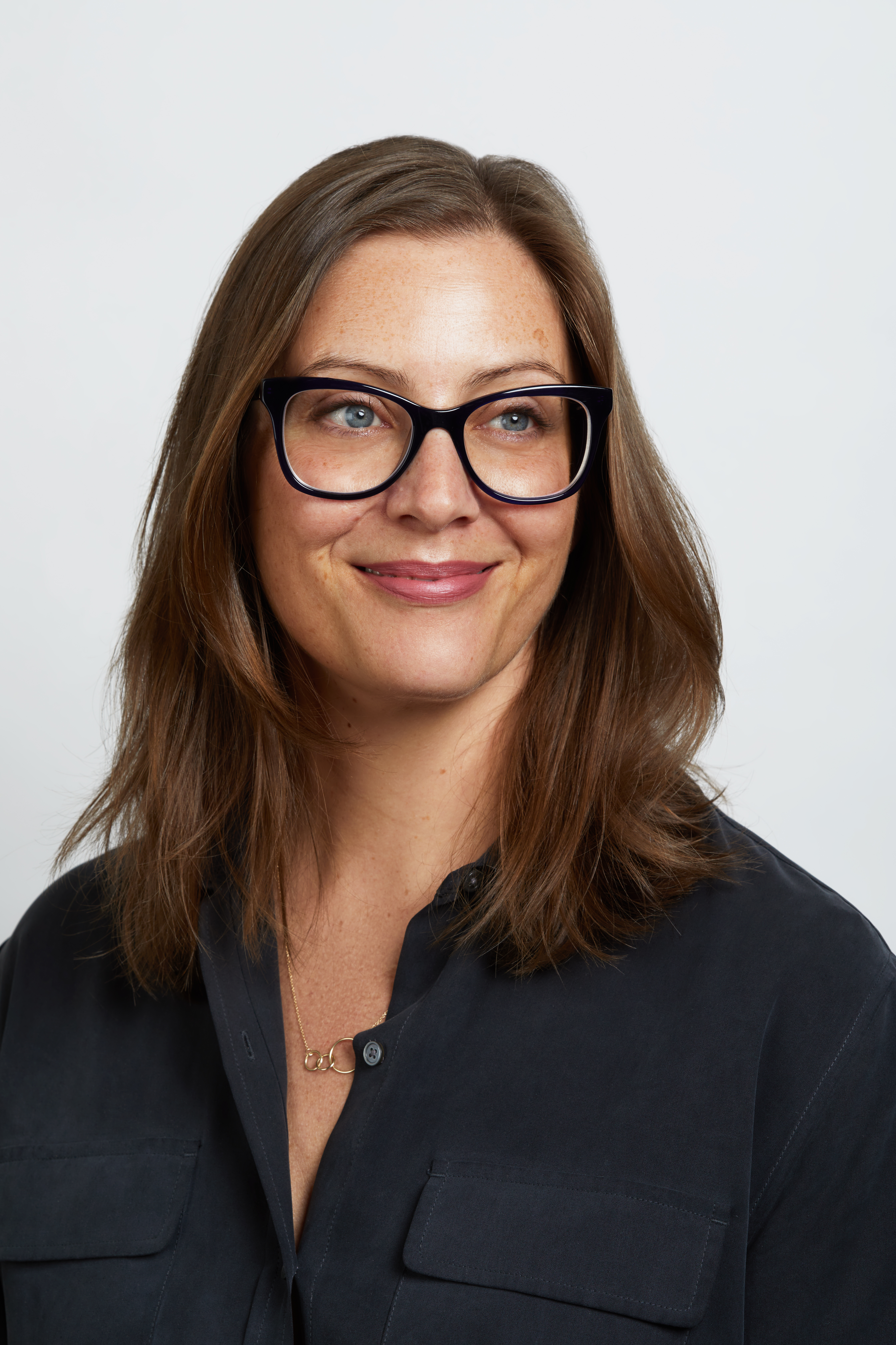 Mulher de cabelo solto loiro-escuro e &oacute;culos preto sorrindo delicadamente sem mostrar os dentes