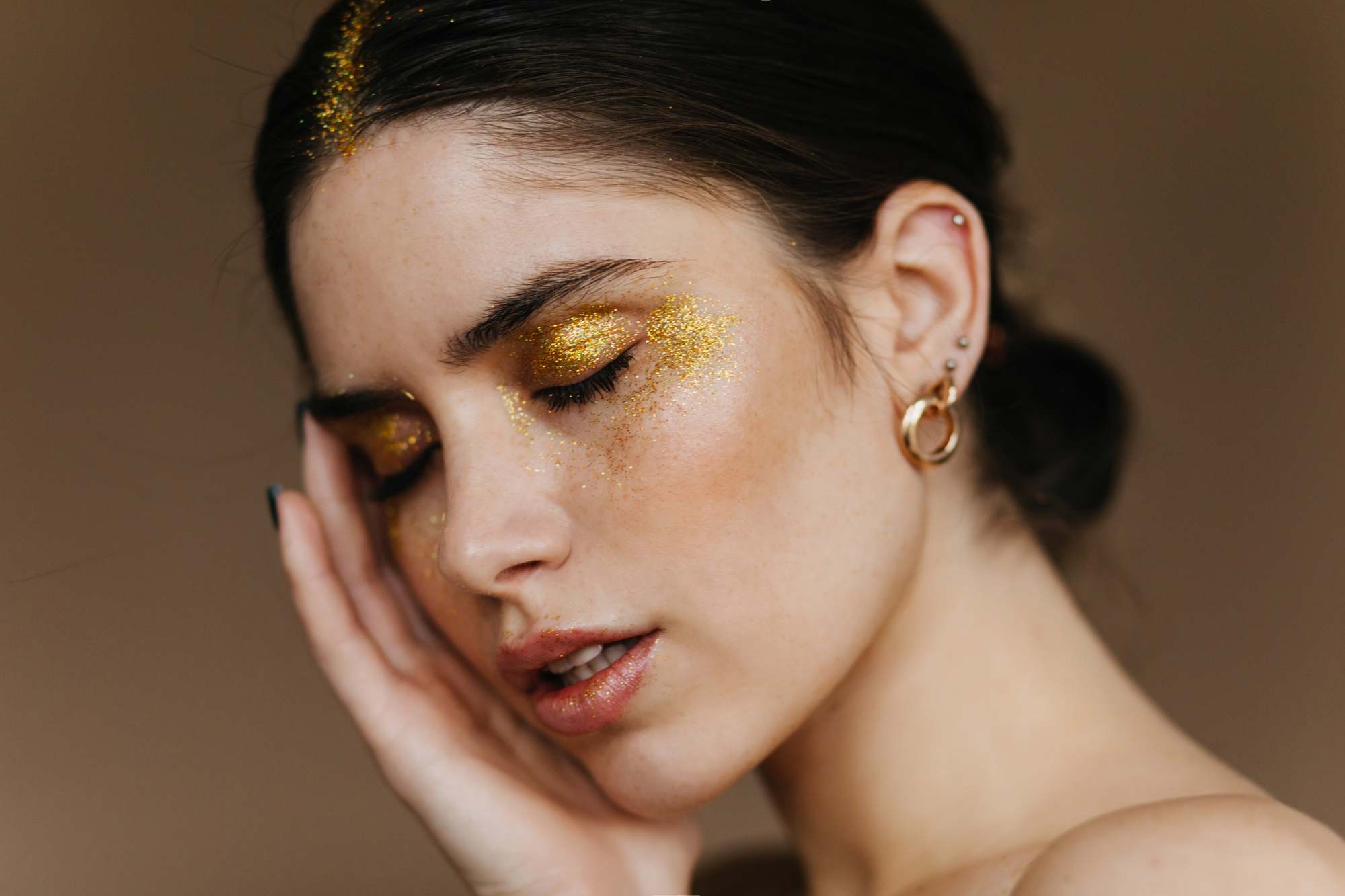 Mulher com maquiagem de Carnaval usando glitter dourado intenso nos olhos e na raiz do cabelo, exemplo de produ&ccedil;&atilde;o com brilho que exige cuidados especiais na hora de remover o glitter da pele e dos fios.
