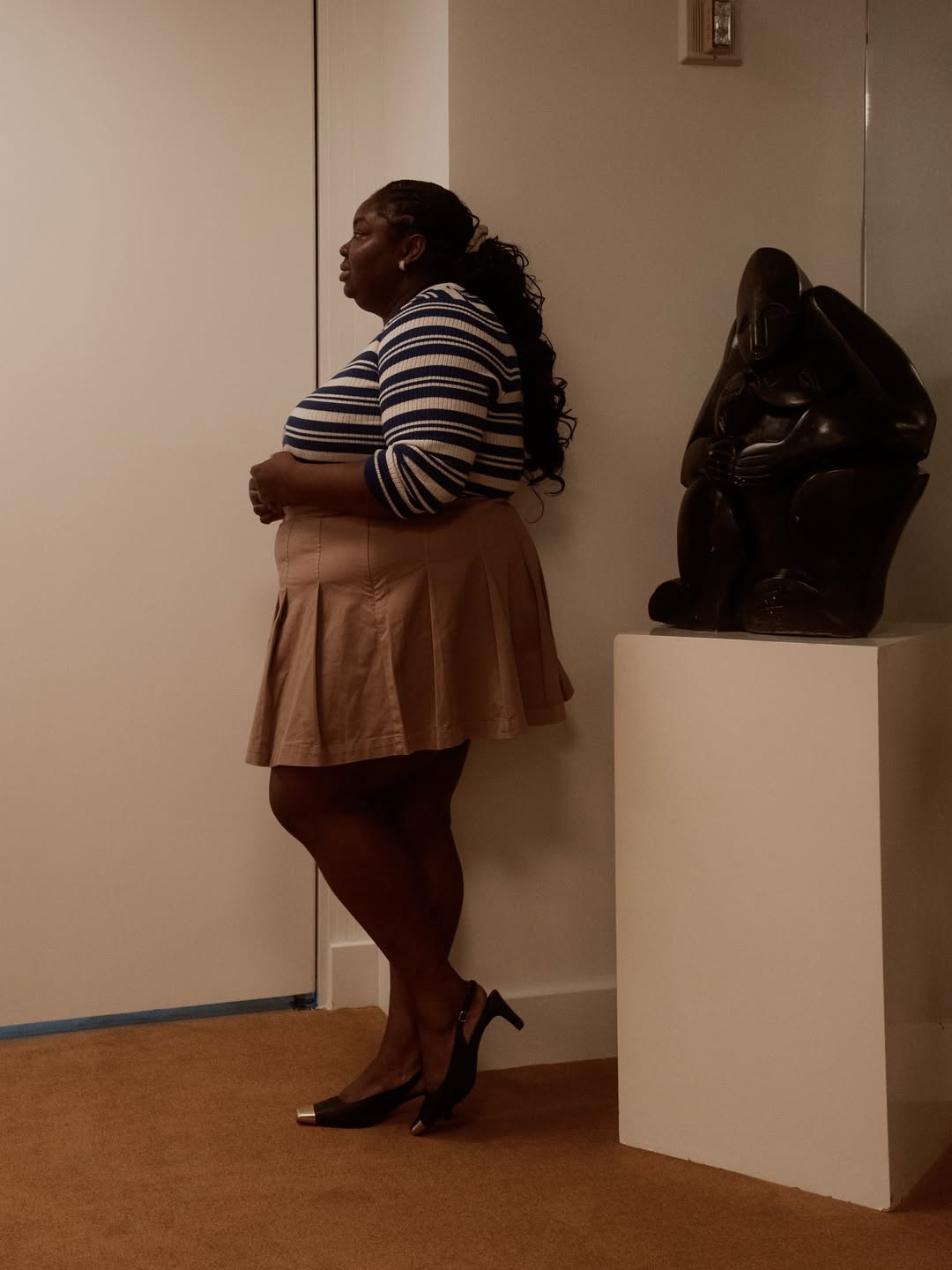 Foto de uma mulher negra usando um look composto por blusa listrada, saia plissada marrom e salto preto