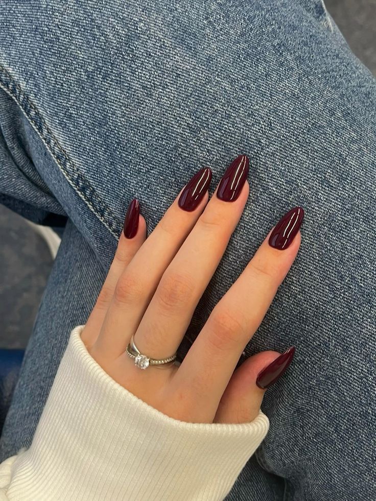 M&atilde;o feminina apoiada sobre pernas cruzadas usando esmalte bord&ocirc;