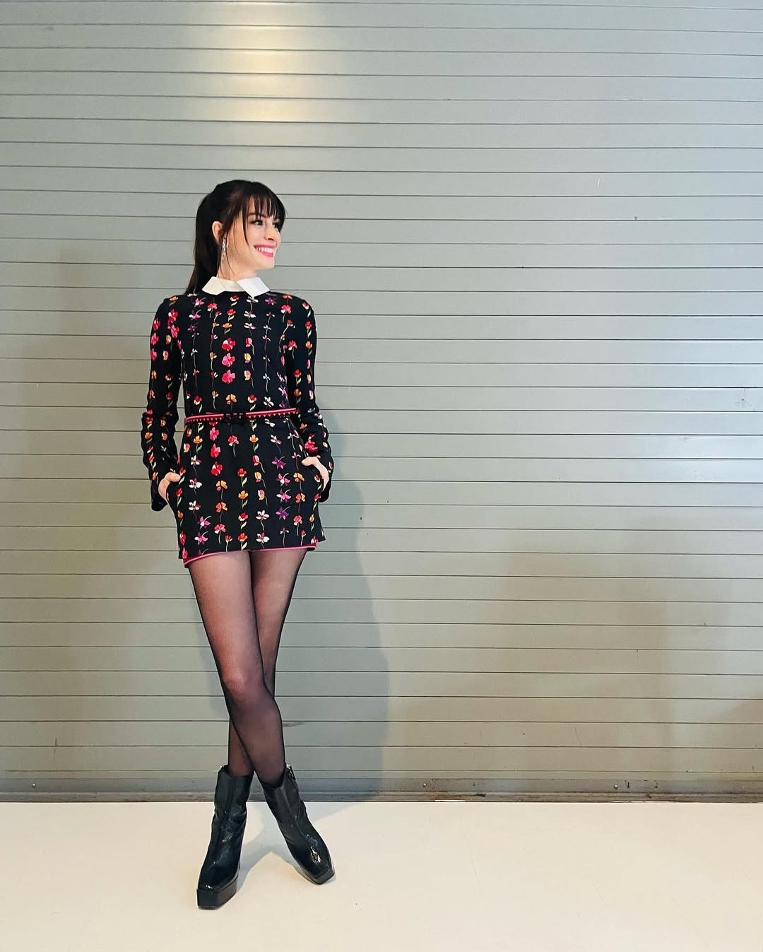 Foto de Anne Hathaway usando um look composto por macaquinho, meia-cal&ccedil;a preta e bota de couro