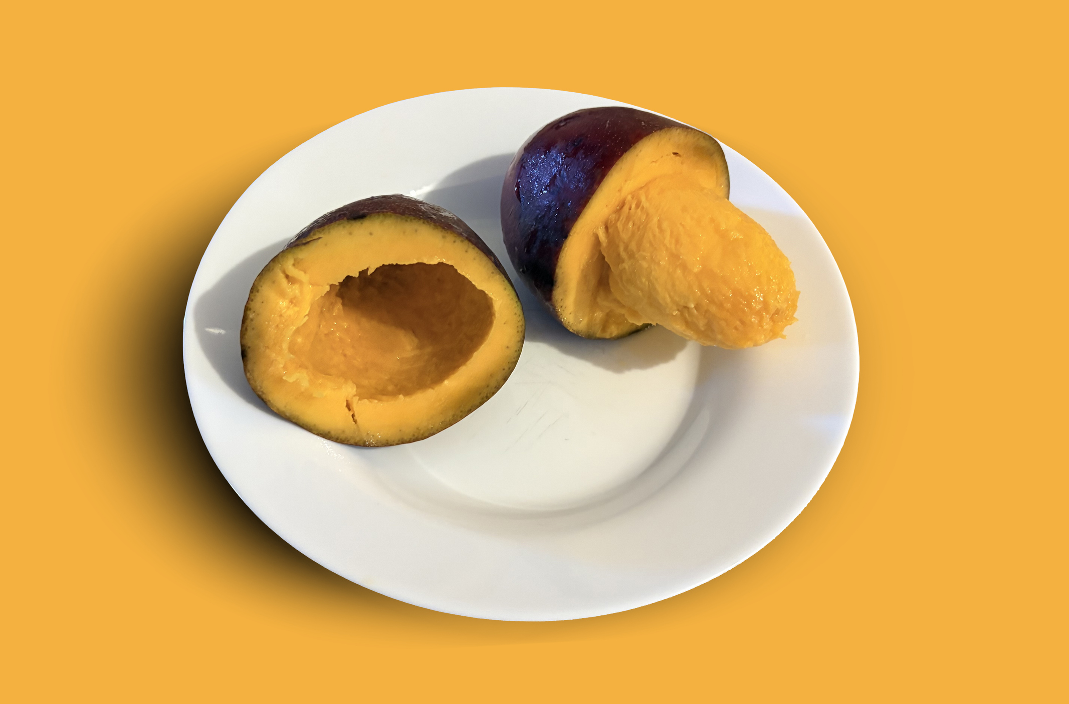 Fruta abiu amarela cortada ao meio em um prato branco, revelando sua polpa cremosa e brilhante, sobre um fundo amarelo vibrante.