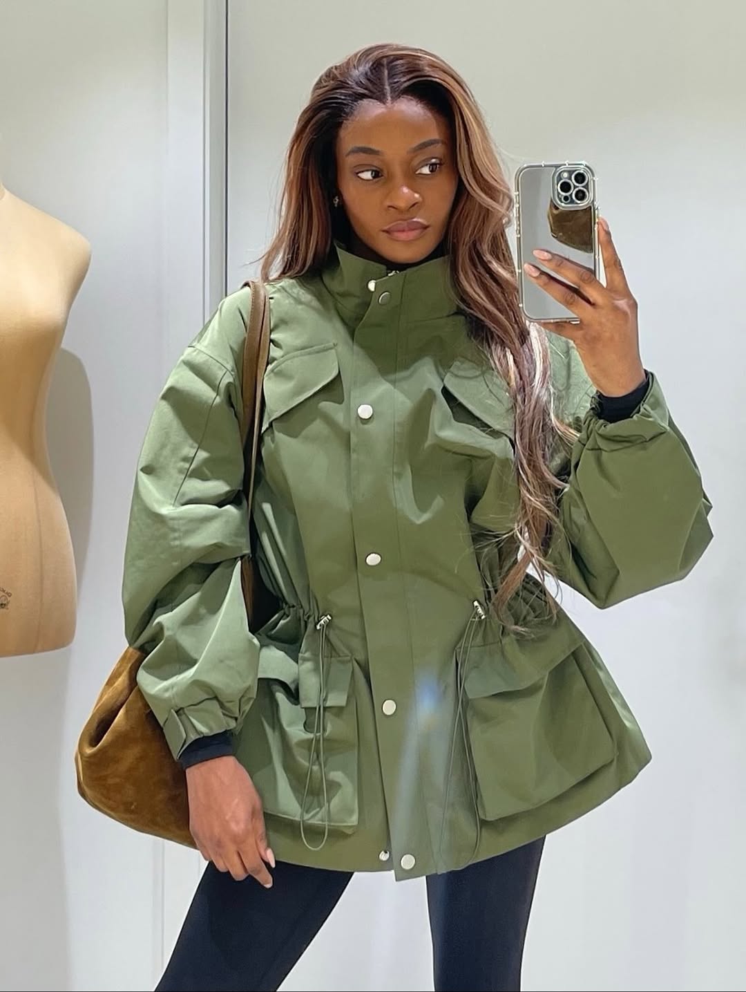 Foto de uma mulher negra usando um look composto por jaqueta parka verde, bolsa marrom e cal&ccedil;a legging