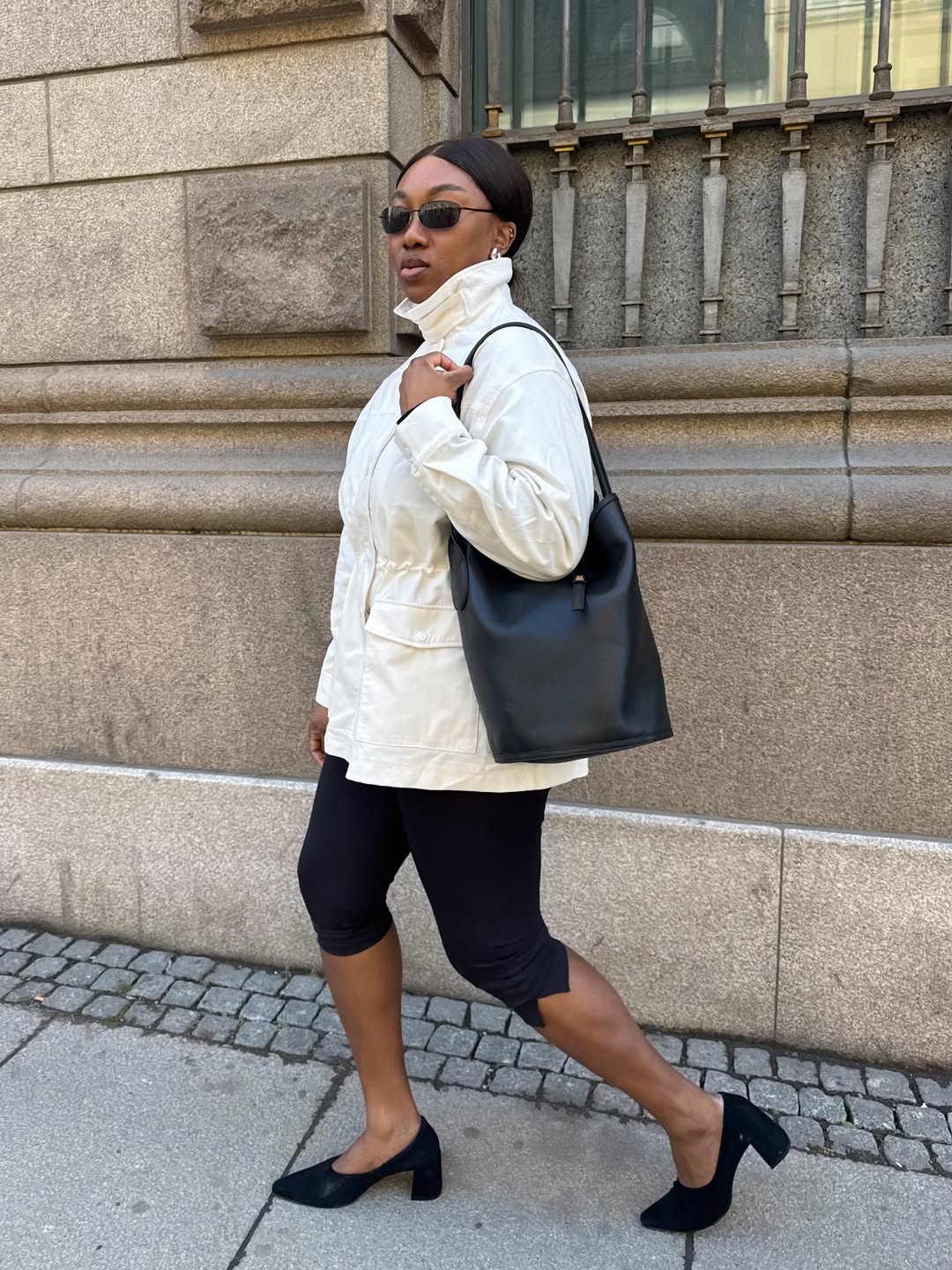 Foto de uma mulher negra usando um look composto por jaqueta parka branca, cal&ccedil;a capri preta e salto
