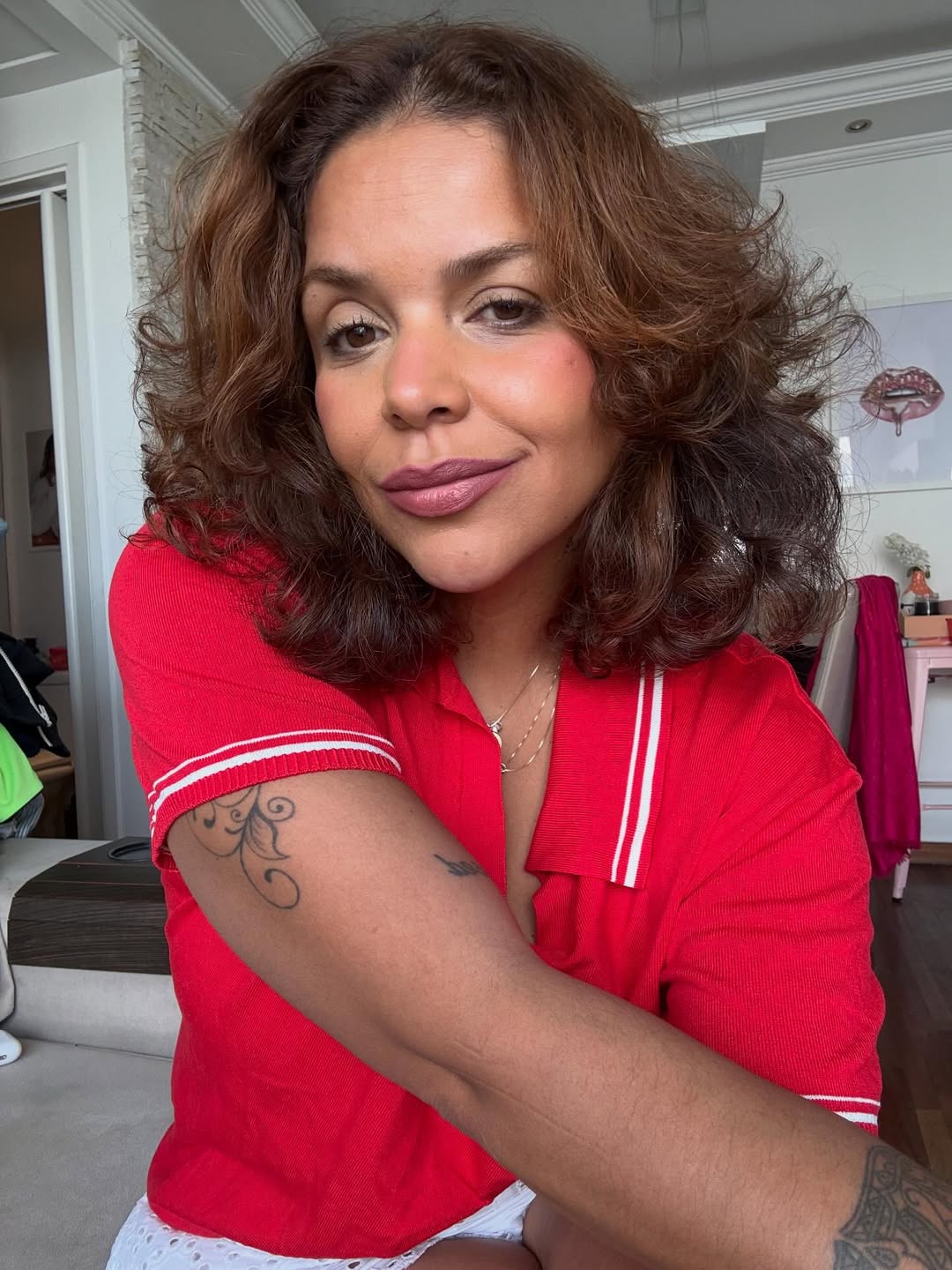 Ju de Paulla aparece sorrindo em selfie descontra&iacute;da dentro de casa, usando camisa vermelha com detalhes brancos e cabelo volumoso. Conhecida pelo humor &aacute;cido nas redes sociais e pelos sets animados, a DJ e influenciadora representa o pop e o funk na programa&ccedil;&atilde;o do C6 Fest.
