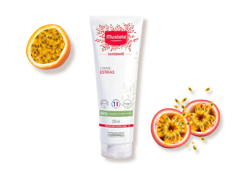 Tubo branco de creme Mustela Maternit&eacute; Creme Estrias, com detalhes em vermelho e verde, ao lado de maracuj&aacute;s cortados ao meio, mostrando a polpa amarela com sementes escuras