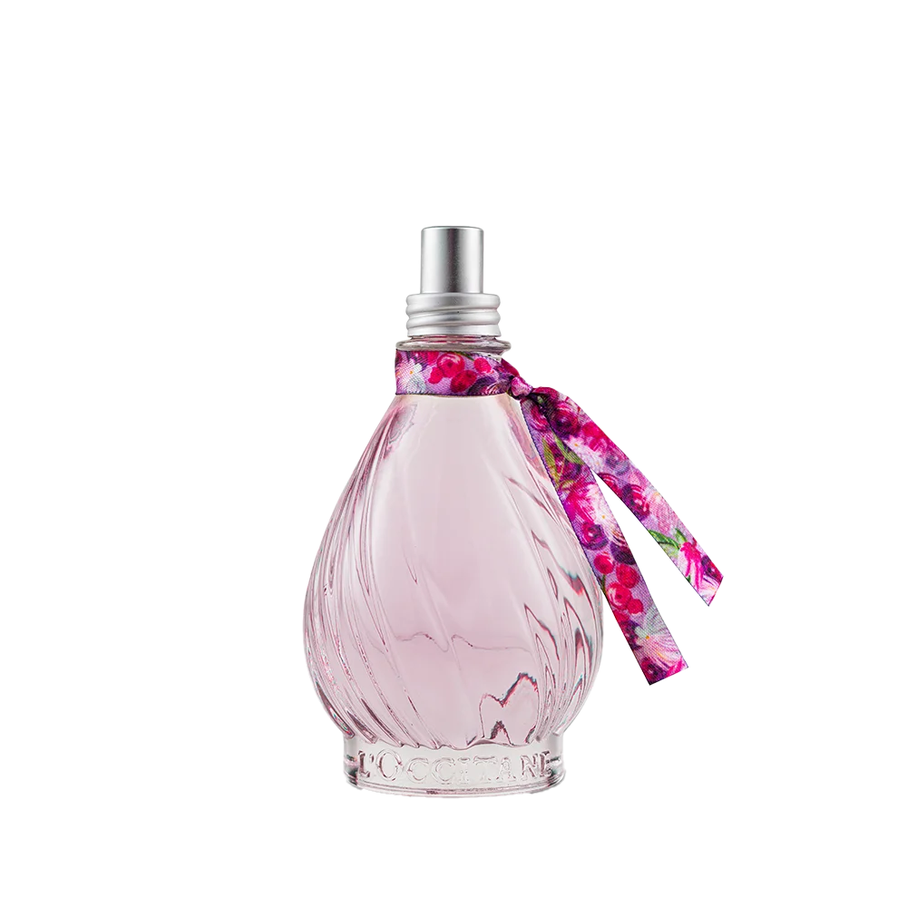 Frasco de perfume LOccitane com l&iacute;quido rosa claro, formato de gota com relevos espirais, tampa prateada e fita floral colorida amarrada no gargalo