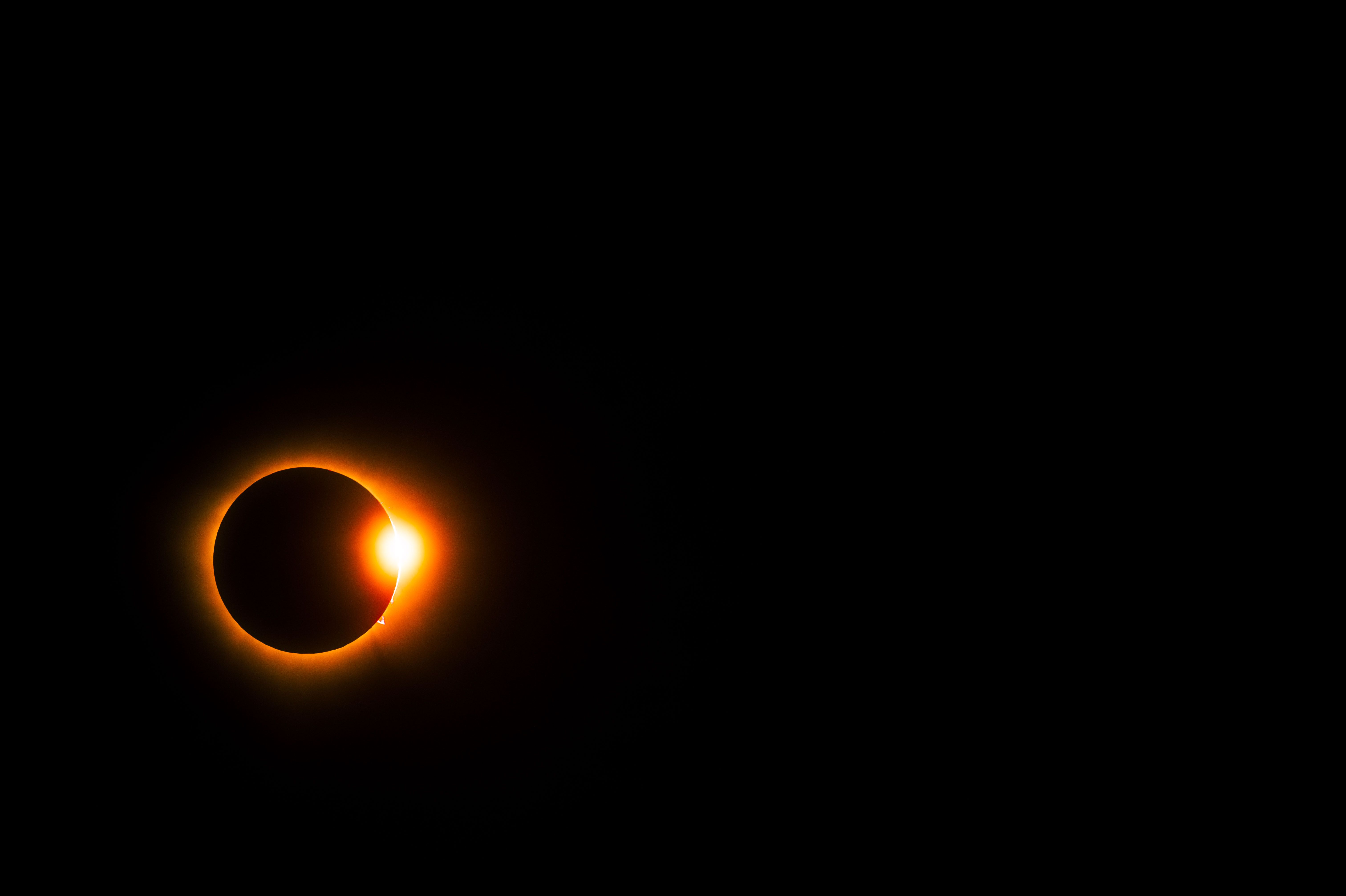 Eclipse solar anular com o Sol quase totalmente coberto pela Lua, formando um anel de luz laranja brilhante ao redor da silhueta escura da Lua, com um ponto de luz intensa no lado direito inferior, em um c&eacute;u noturno escuro