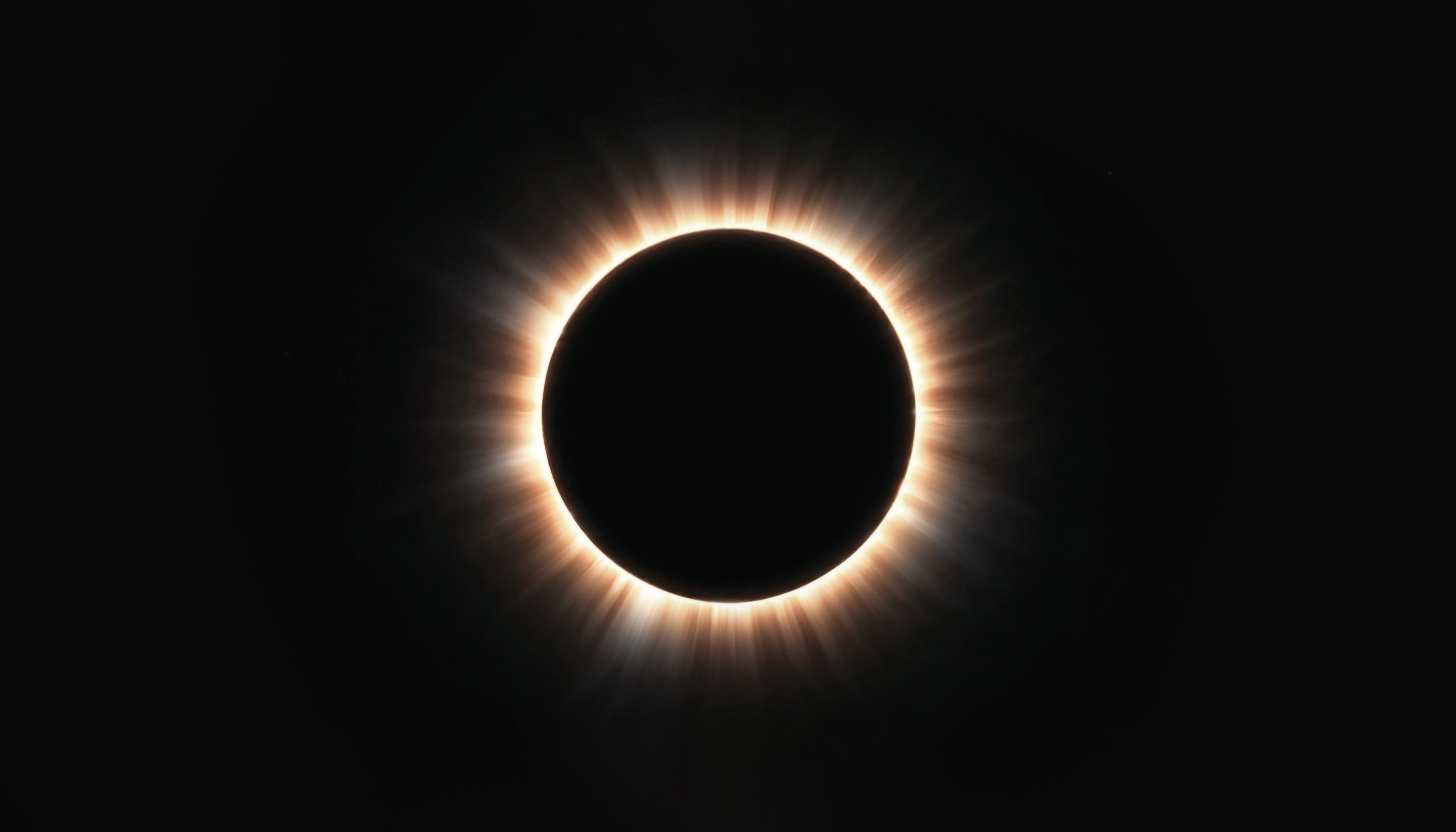 Eclipse solar total com a Lua cobrindo o Sol, revelando a coroa solar brilhante e alaranjada em um céu escuro