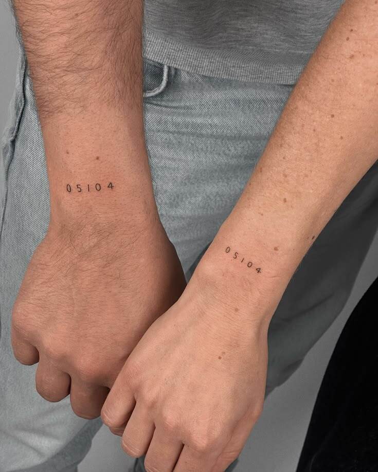 Dois pulsos, um masculino e um feminino, lado a lado, exibindo tatuagens id&ecirc;nticas com os n&uacute;meros 05104 em fonte fina e preta